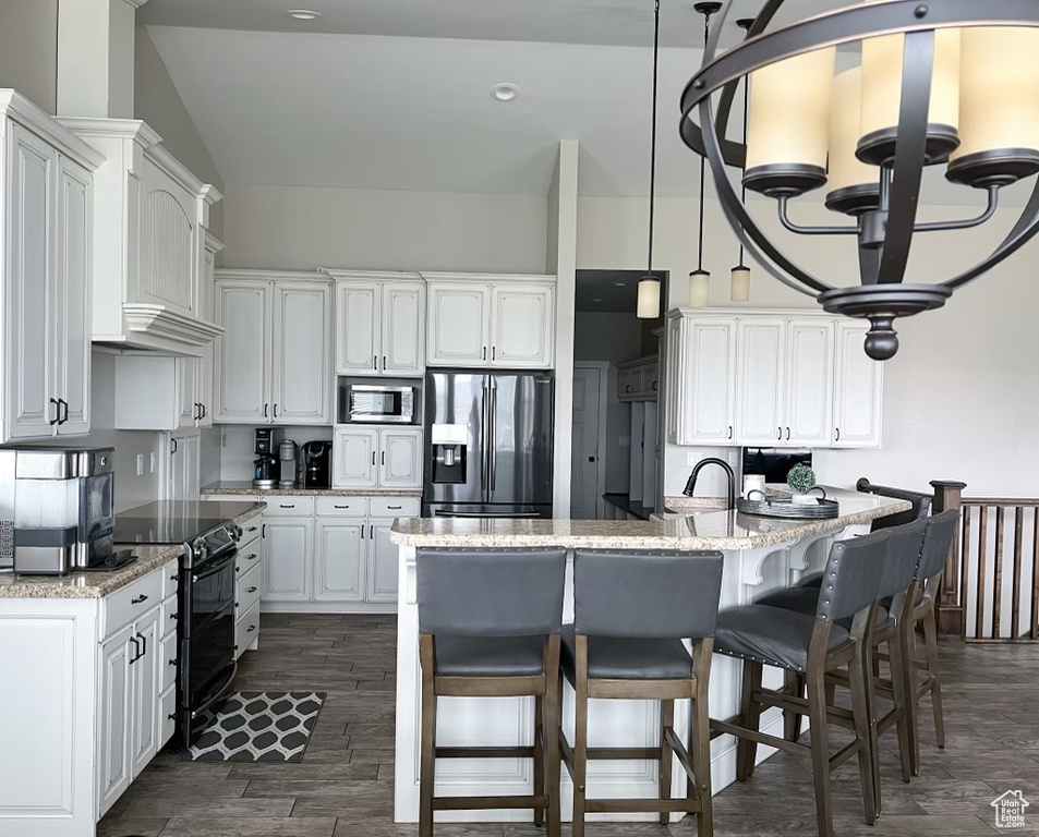 Kitchen featuring hanging light fixtures, white cabinetry, a kitchen island with sink, stainless steel appliances, and light stone counters