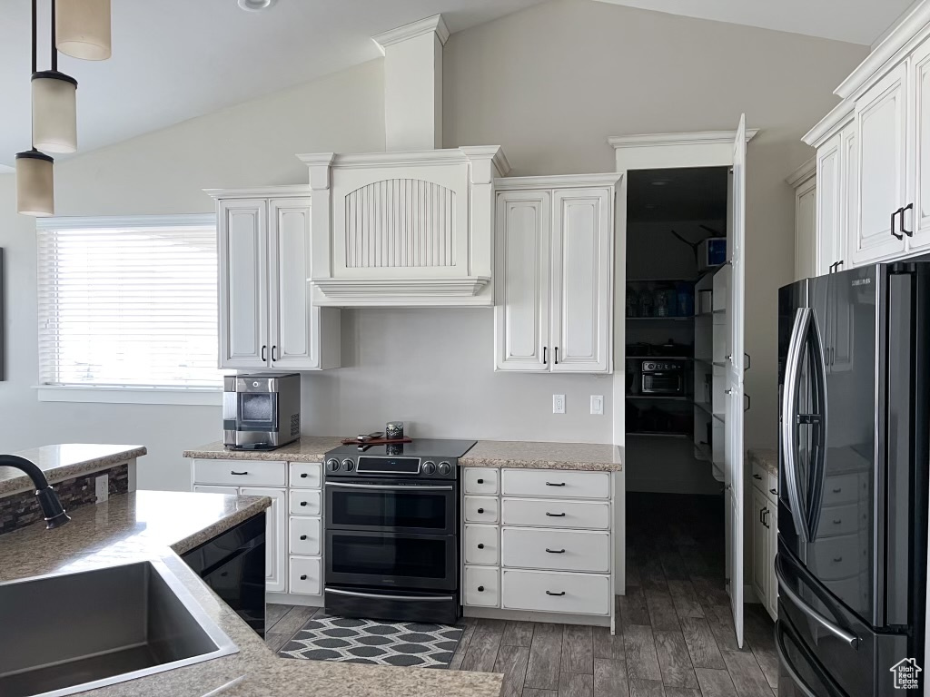 Kitchen with black refrigerator, lofted ceiling, white cabinetry, sink, and range with two ovens