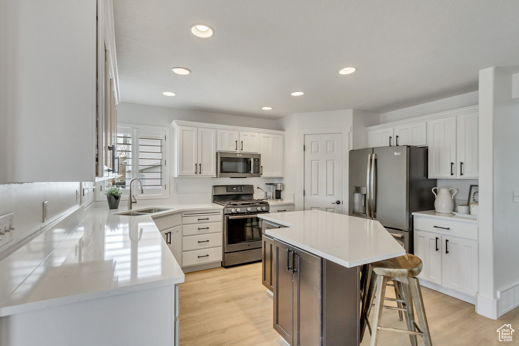 Kitchen with appliances with stainless steel finishes, white cabinets, light hardwood / wood-style flooring, a center island, and sink