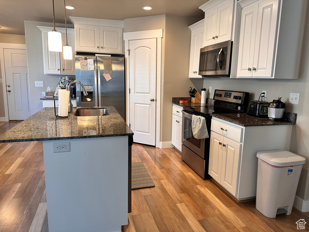 Kitchen featuring appliances with stainless steel finishes, light hardwood / wood-style flooring, white cabinets, dark stone counters, and pendant lighting