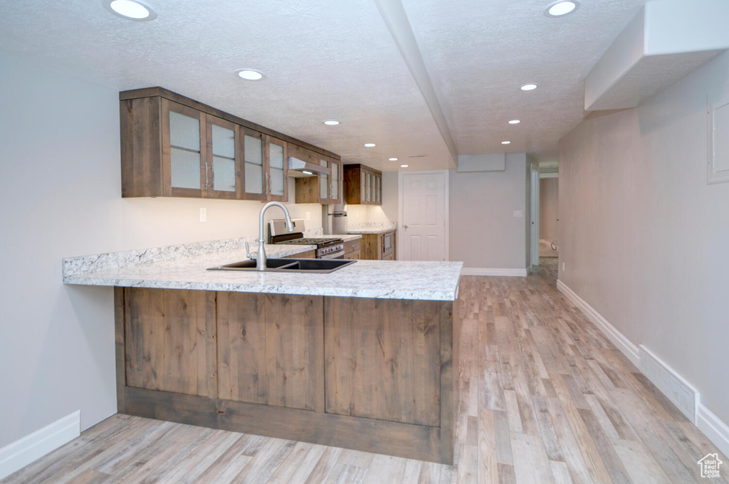 Kitchen featuring sink, a textured ceiling, light hardwood / wood-style floors, and light stone counters