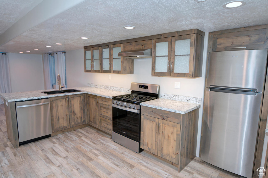 Kitchen with stainless steel appliances, kitchen peninsula, light hardwood / wood-style flooring, wall chimney range hood, and sink