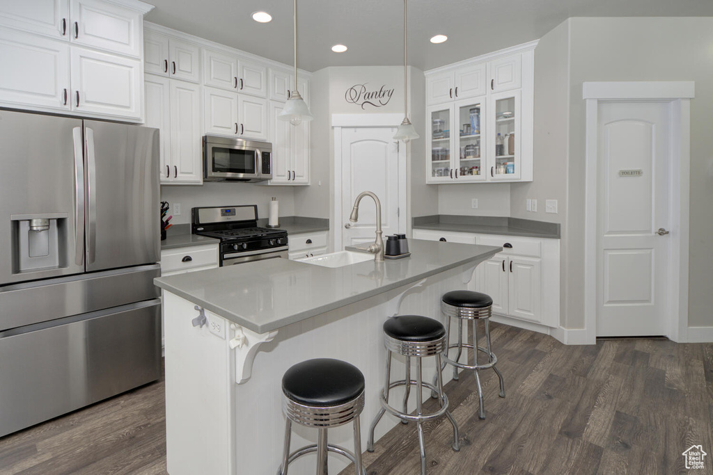 Kitchen featuring decorative light fixtures, appliances with stainless steel finishes, white cabinets, and a kitchen island with sink