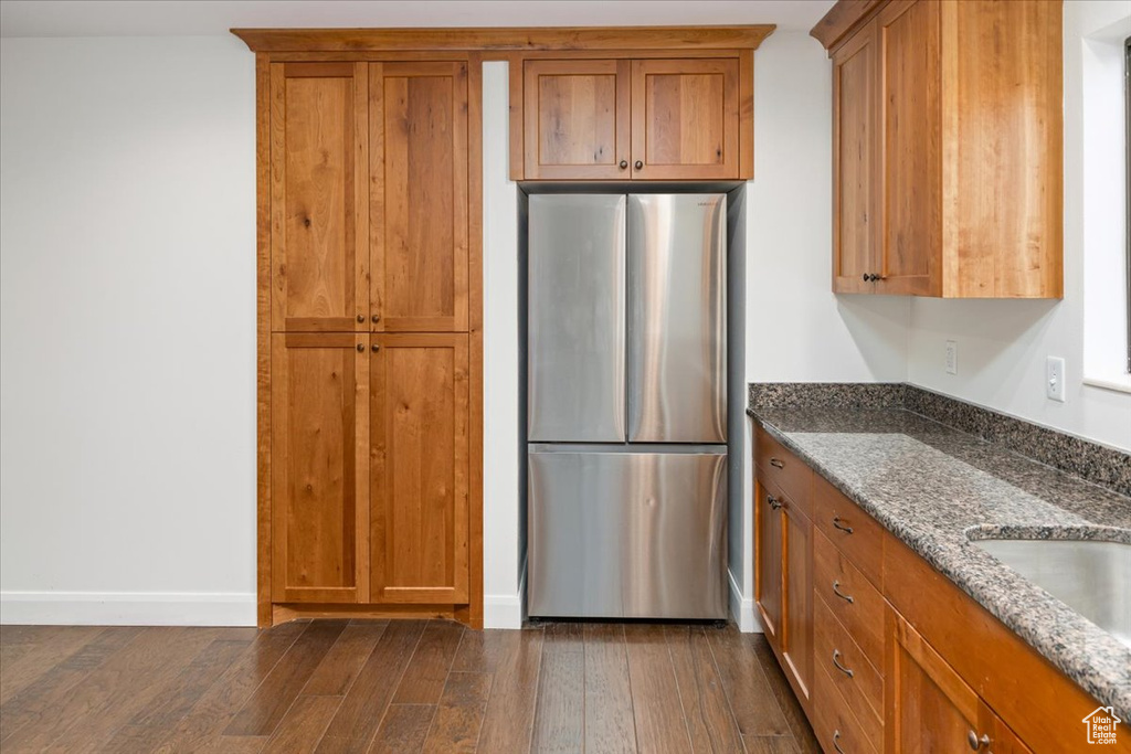 Kitchen featuring dark stone counters, dark wood-type flooring, and stainless steel refrigerator