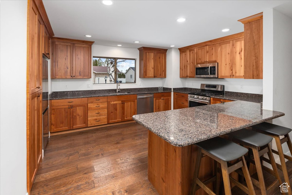 Kitchen featuring kitchen peninsula, dark hardwood / wood-style floors, a kitchen breakfast bar, appliances with stainless steel finishes, and dark stone countertops