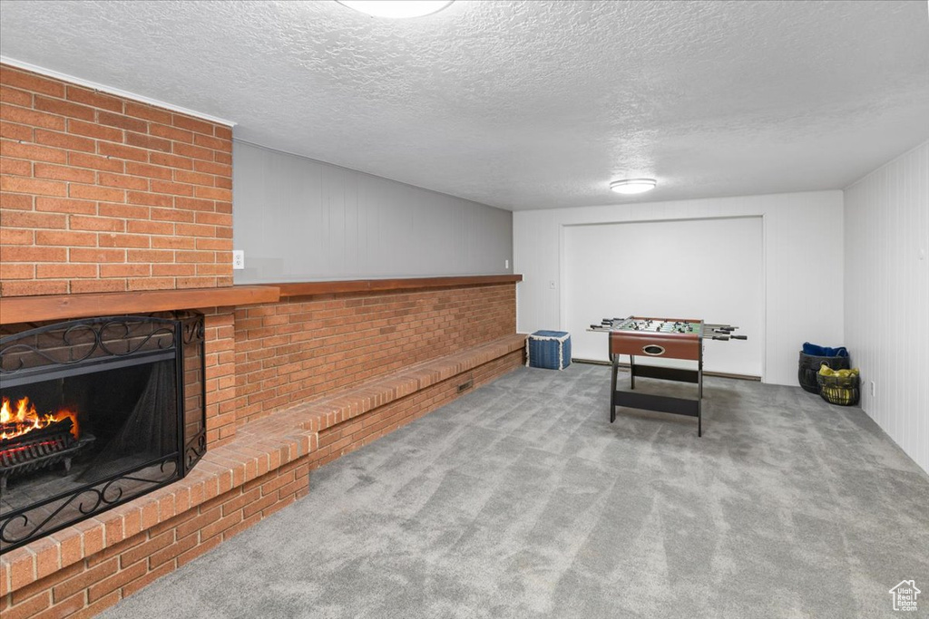 Recreation room featuring a textured ceiling, carpet, and a brick fireplace
