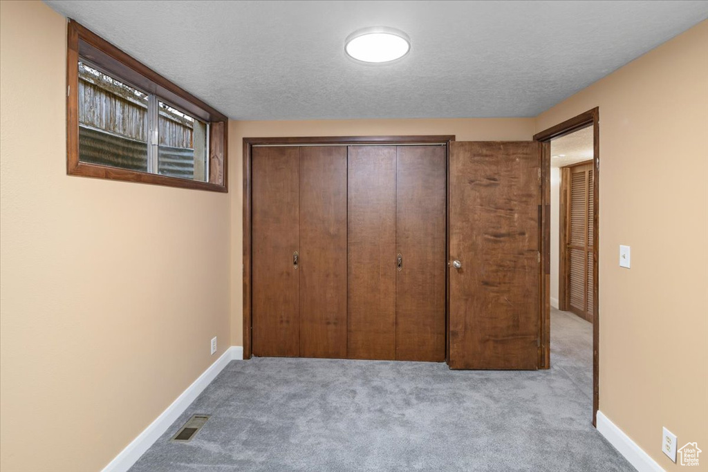 Unfurnished bedroom with light carpet, a closet, and a textured ceiling