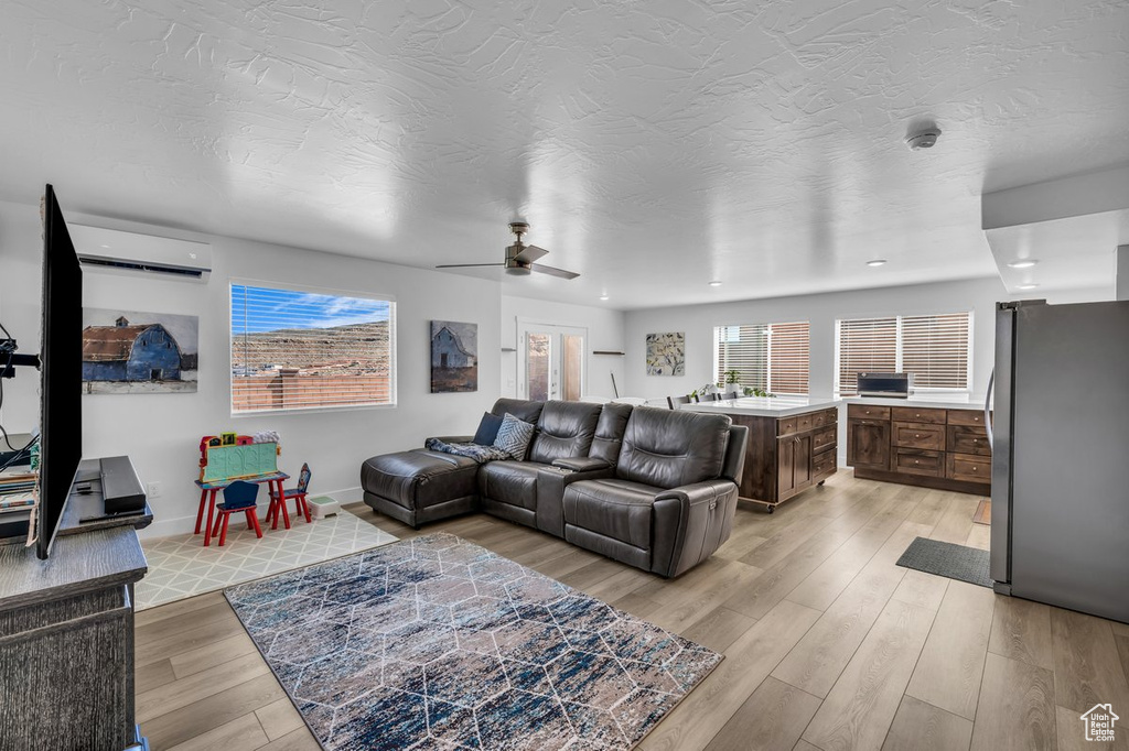 Living room featuring light hardwood / wood-style floors, ceiling fan, and a wall unit AC
