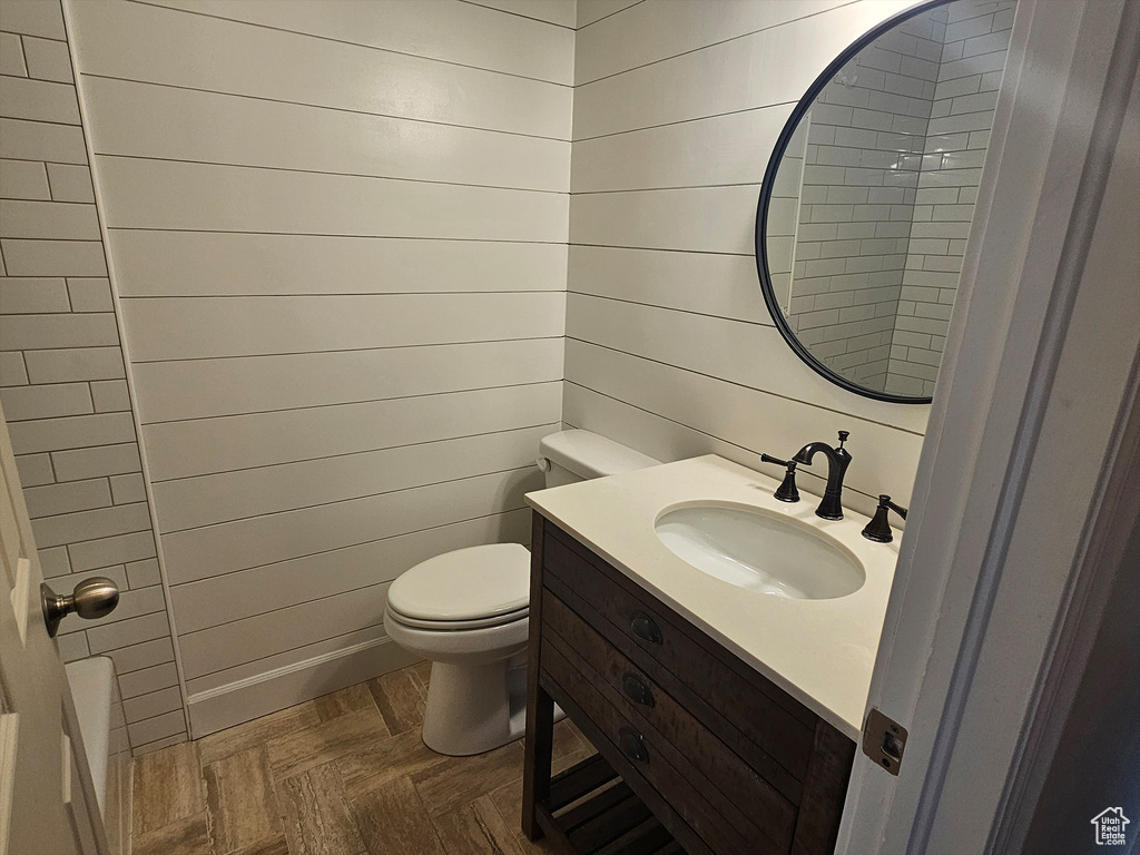 Bathroom with wooden walls, toilet, parquet flooring, and vanity