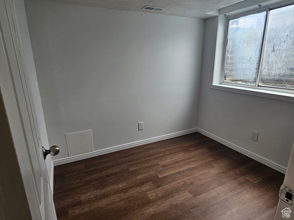 Empty room with a textured ceiling and dark hardwood / wood-style flooring