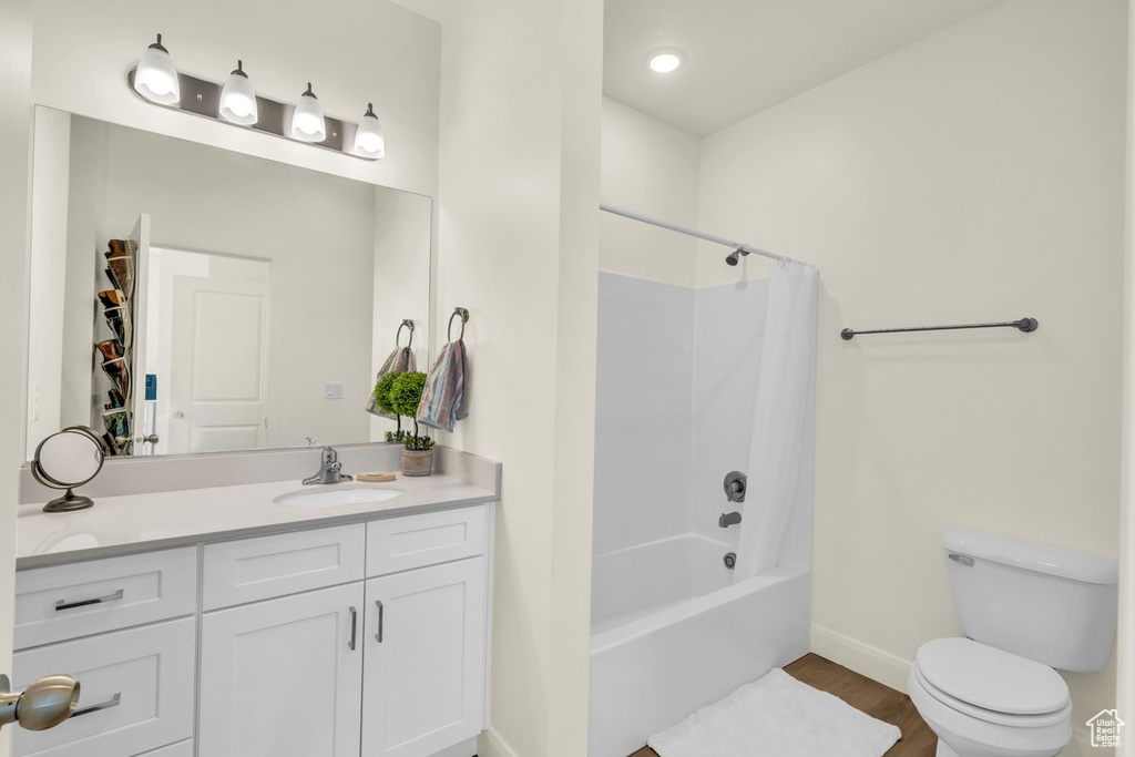Full bathroom with vanity, shower / bath combo with shower curtain, hardwood / wood-style floors, and toilet
