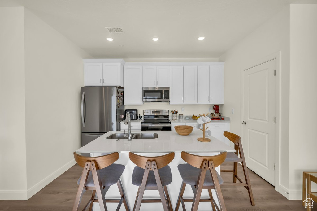 Kitchen featuring white cabinetry, dark wood-type flooring, sink, stainless steel appliances, and a center island with sink