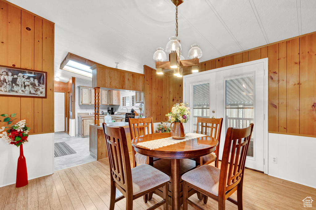 Dining room featuring light hardwood / wood-style flooring, an inviting chandelier, wood walls, and lofted ceiling