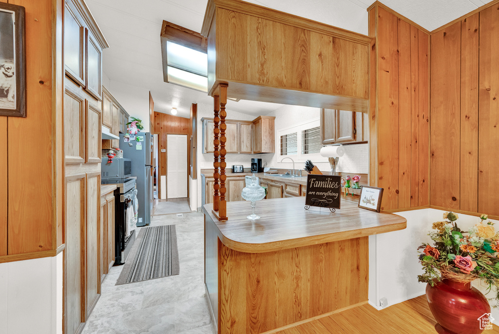 Kitchen with wood walls, range, kitchen peninsula, light wood-type flooring, and sink