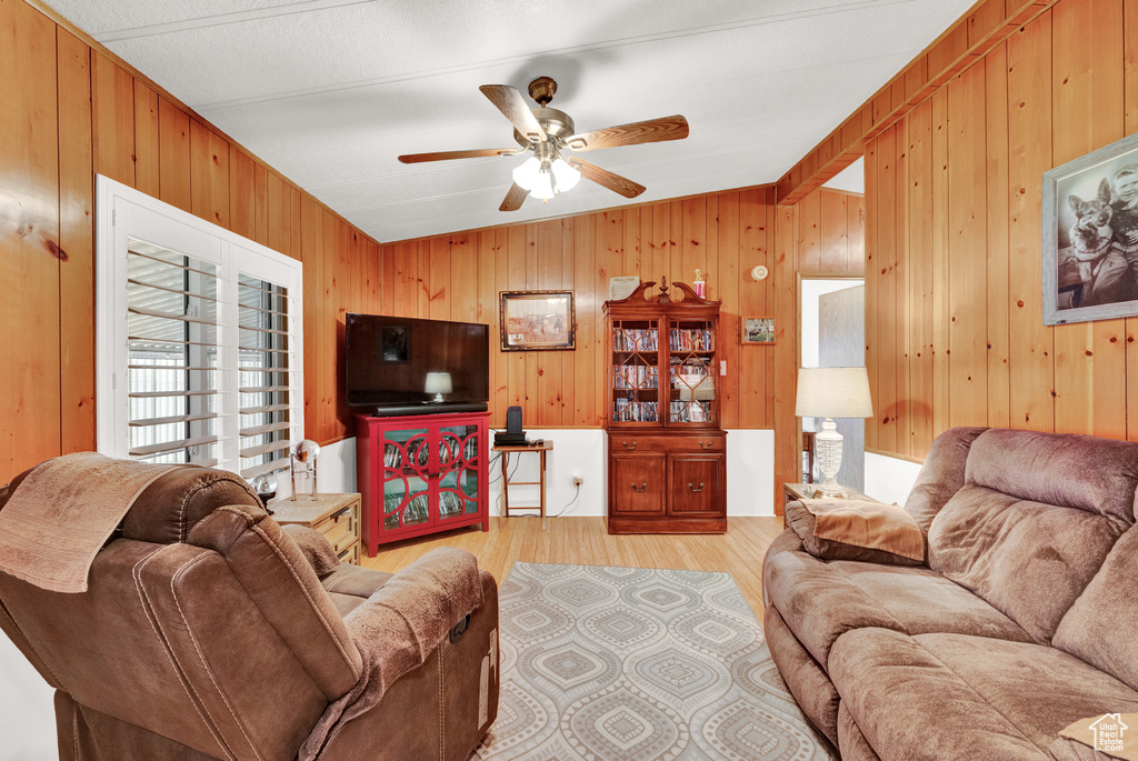 Living room with ceiling fan, wood walls, and light wood-type flooring