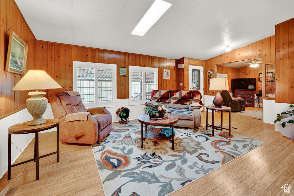 Living room with ceiling fan, wood walls, light hardwood / wood-style flooring, and vaulted ceiling