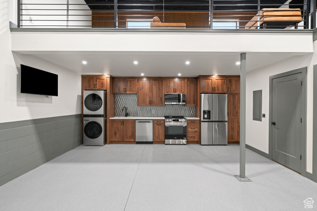 Kitchen featuring backsplash, stacked washing maching and dryer, stainless steel appliances, and sink