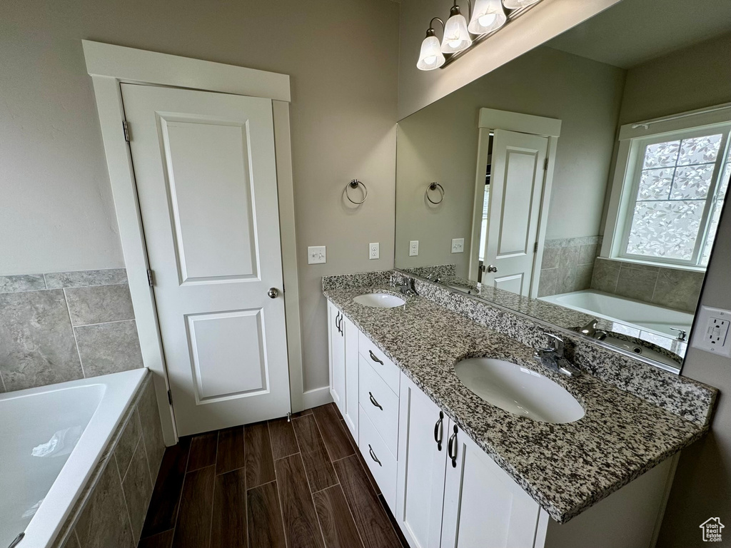 Bathroom featuring tiled bath, large vanity, and dual sinks