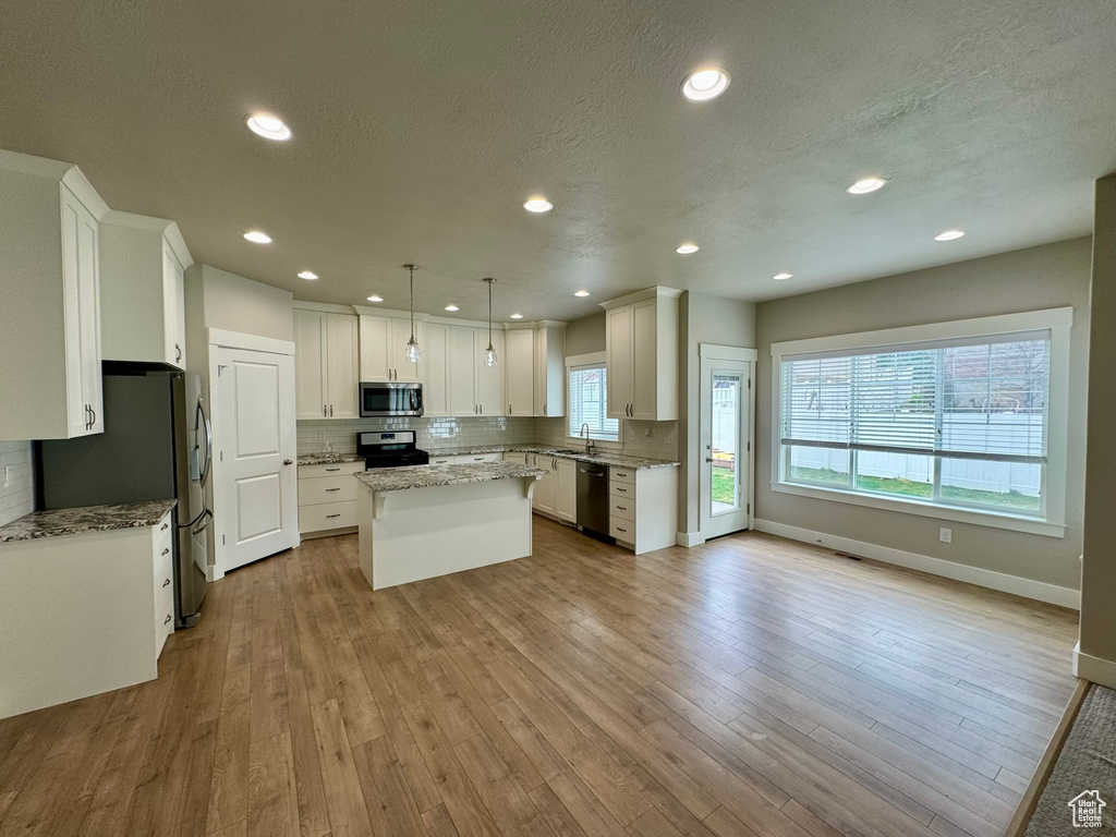Kitchen featuring a center island, stainless steel appliances, decorative light fixtures, white cabinetry, and light hardwood / wood-style flooring