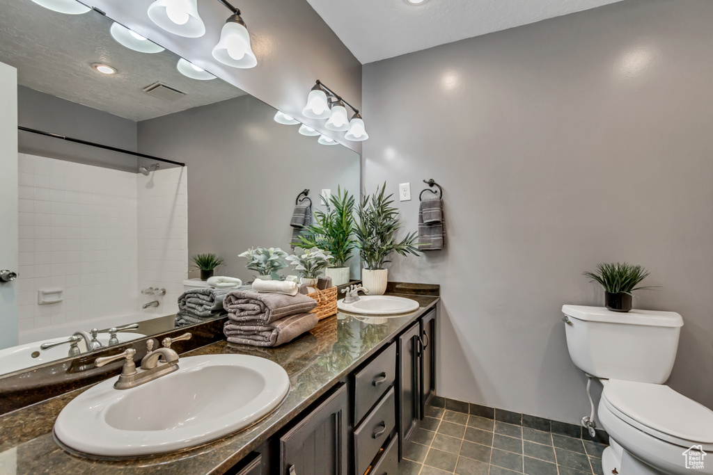 Full bathroom featuring toilet, large vanity, washtub / shower combination, dual sinks, and tile floors