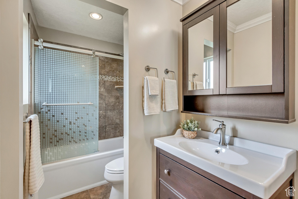 Full bathroom with tile flooring, vanity with extensive cabinet space, toilet, crown molding, and enclosed tub / shower combo