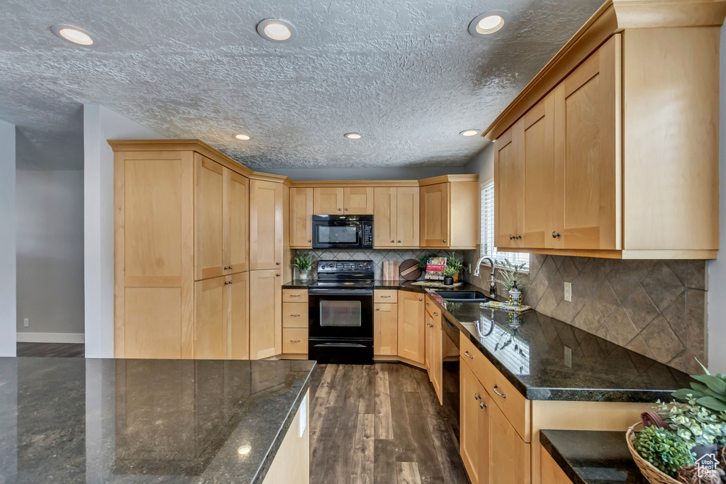 Kitchen with light brown cabinetry, backsplash, dark stone countertops, dark hardwood / wood-style flooring, and black appliances