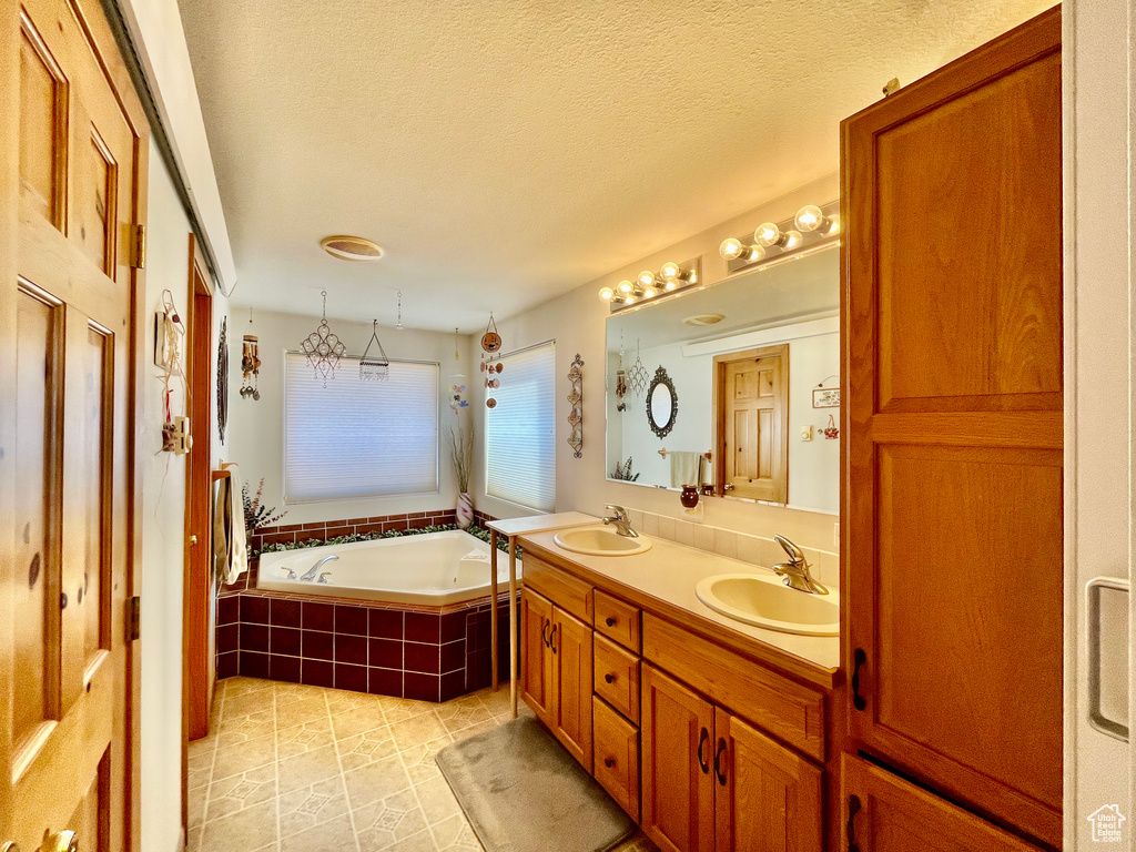 Bathroom with dual vanity, a textured ceiling, tile floors, and tiled tub