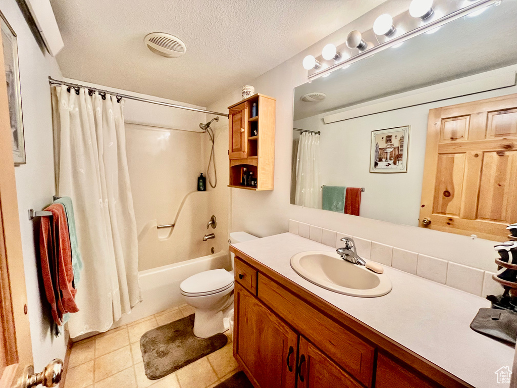 Full bathroom featuring vanity, shower / tub combo with curtain, a textured ceiling, tile flooring, and toilet