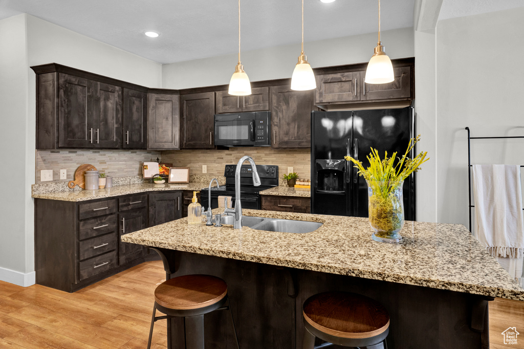 Kitchen featuring hanging light fixtures, black appliances, light hardwood / wood-style floors, tasteful backsplash, and dark brown cabinetry