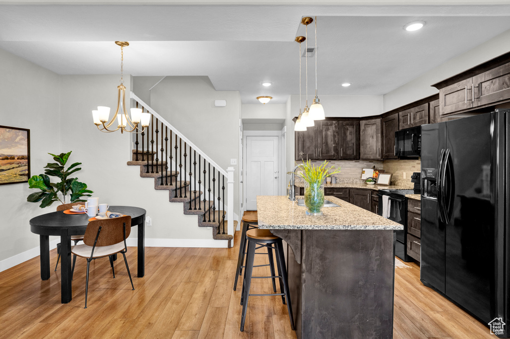 Kitchen featuring a chandelier, light stone countertops, black appliances, hanging light fixtures, and light wood-type flooring
