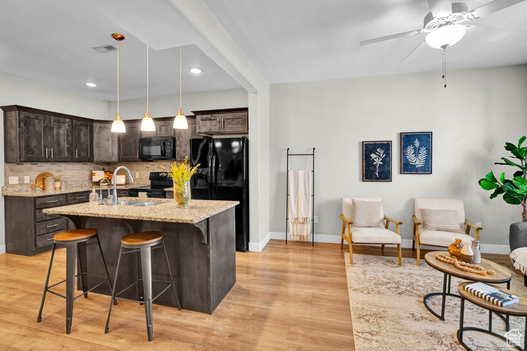 Kitchen with light stone countertops, ceiling fan, tasteful backsplash, black appliances, and hanging light fixtures