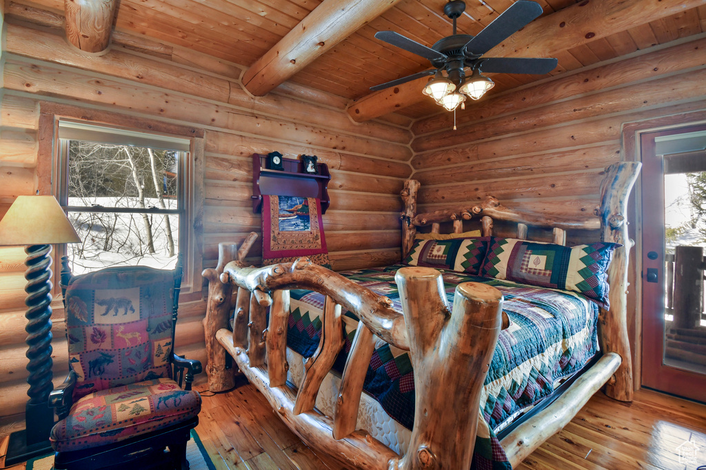 Bedroom with beam ceiling, log walls, multiple windows, and light hardwood / wood-style flooring