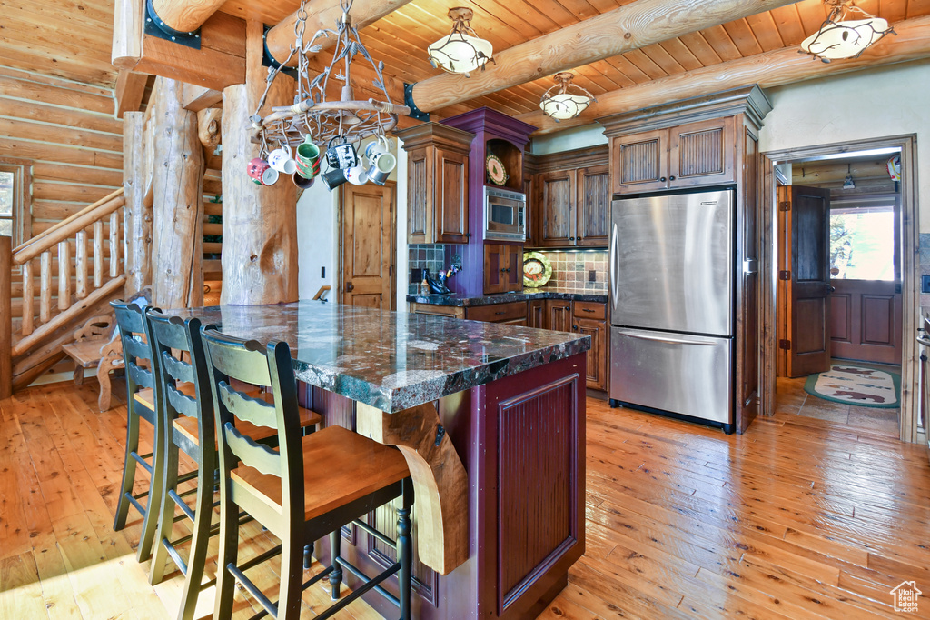 Kitchen with light hardwood / wood-style flooring, log walls, decorative light fixtures, and appliances with stainless steel finishes