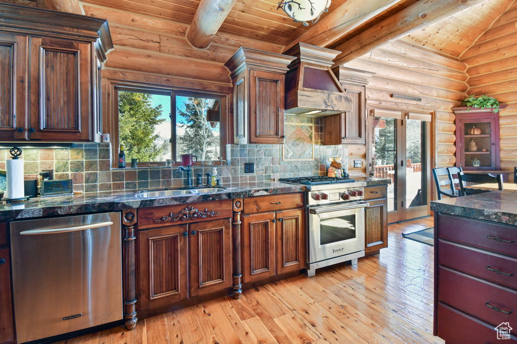 Kitchen with stainless steel appliances, custom exhaust hood, log walls, light hardwood / wood-style flooring, and lofted ceiling
