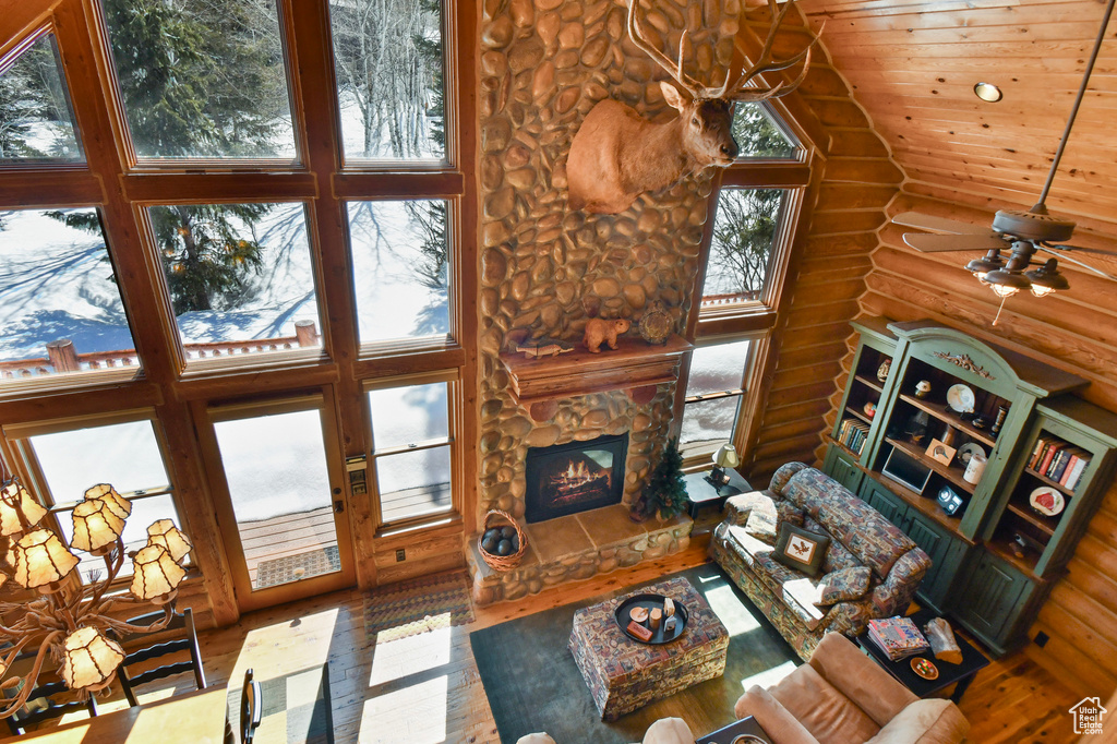 Living room with log walls, ceiling fan, wood-type flooring, high vaulted ceiling, and a stone fireplace