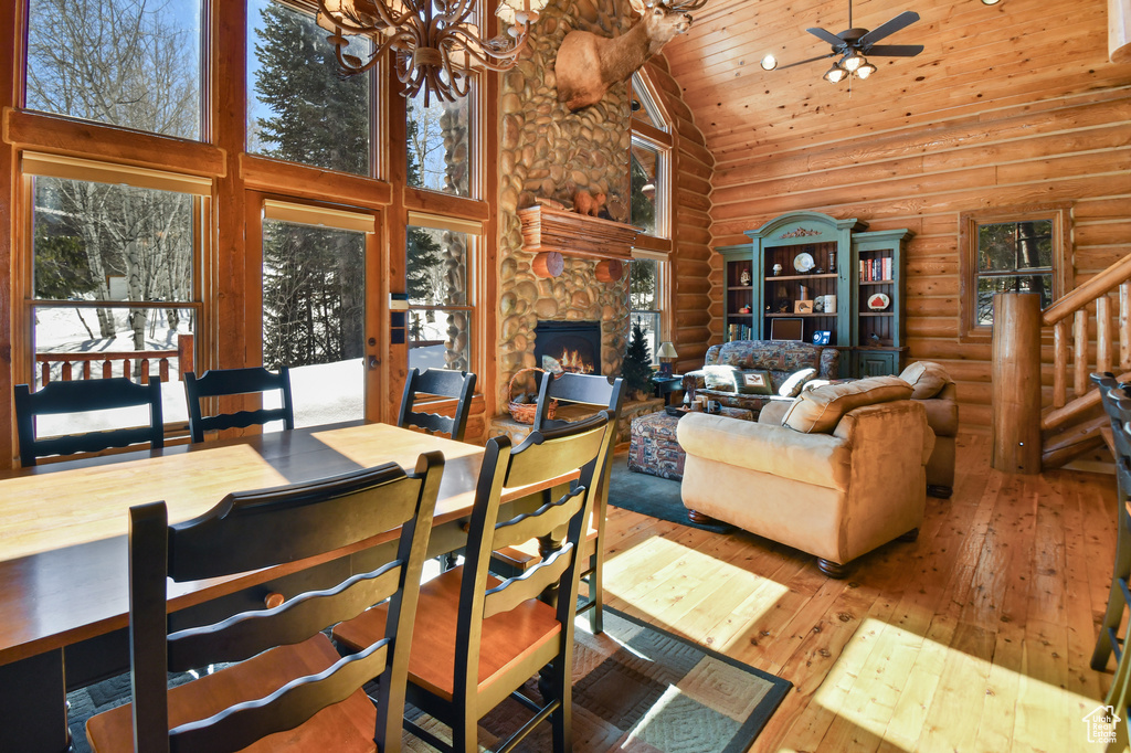 Dining area featuring high vaulted ceiling, wooden ceiling, ceiling fan with notable chandelier, a stone fireplace, and light hardwood / wood-style flooring