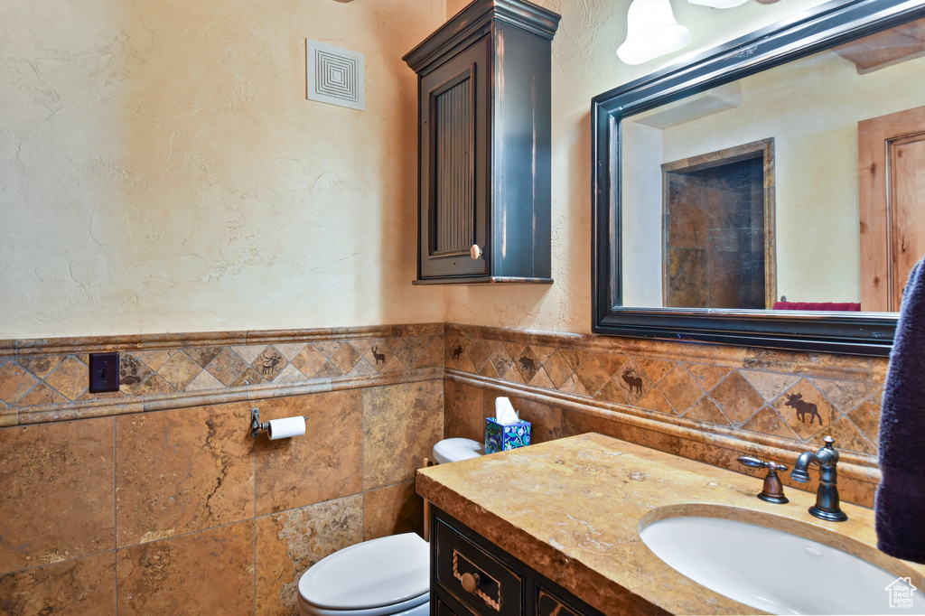 Bathroom with backsplash, toilet, vanity, and tile walls