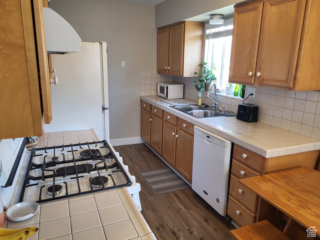 Kitchen with white appliances, backsplash, tile countertops, dark hardwood / wood-style floors, and sink