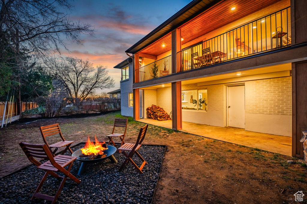 Yard at dusk with an outdoor fire pit, a balcony, and a patio area