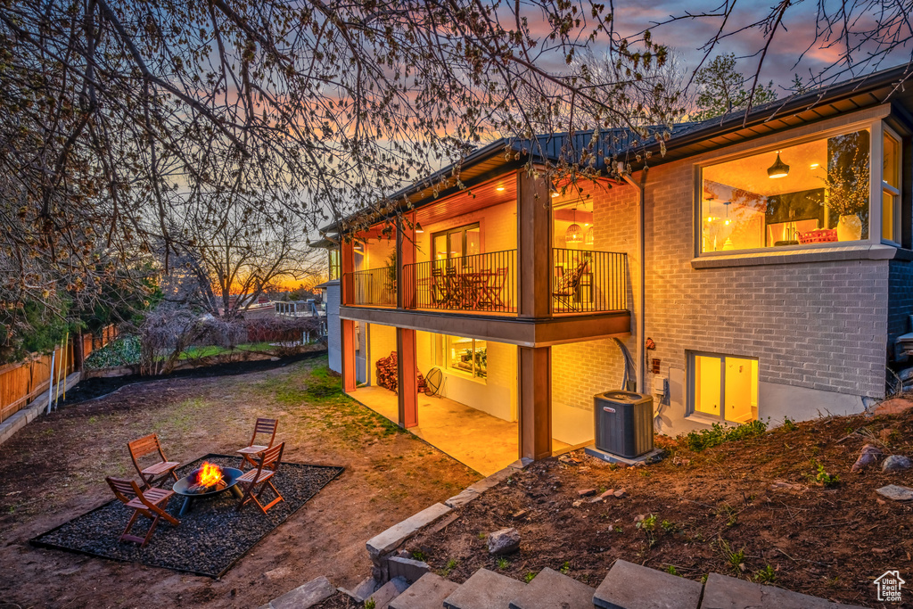 Back house at dusk with central air condition unit, a fire pit, a balcony, and a patio area