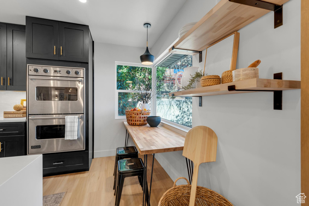 Kitchen featuring stainless steel double oven, light hardwood / wood-style flooring, decorative light fixtures, and backsplash