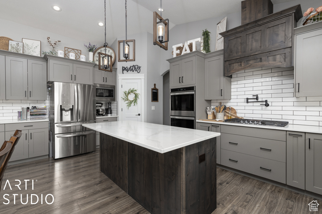Kitchen with decorative light fixtures, a center island, dark wood-type flooring, appliances with stainless steel finishes, and backsplash