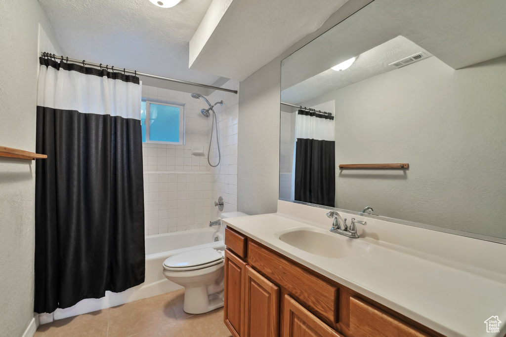Full bathroom with tile floors, a textured ceiling, shower / tub combo, toilet, and vanity with extensive cabinet space