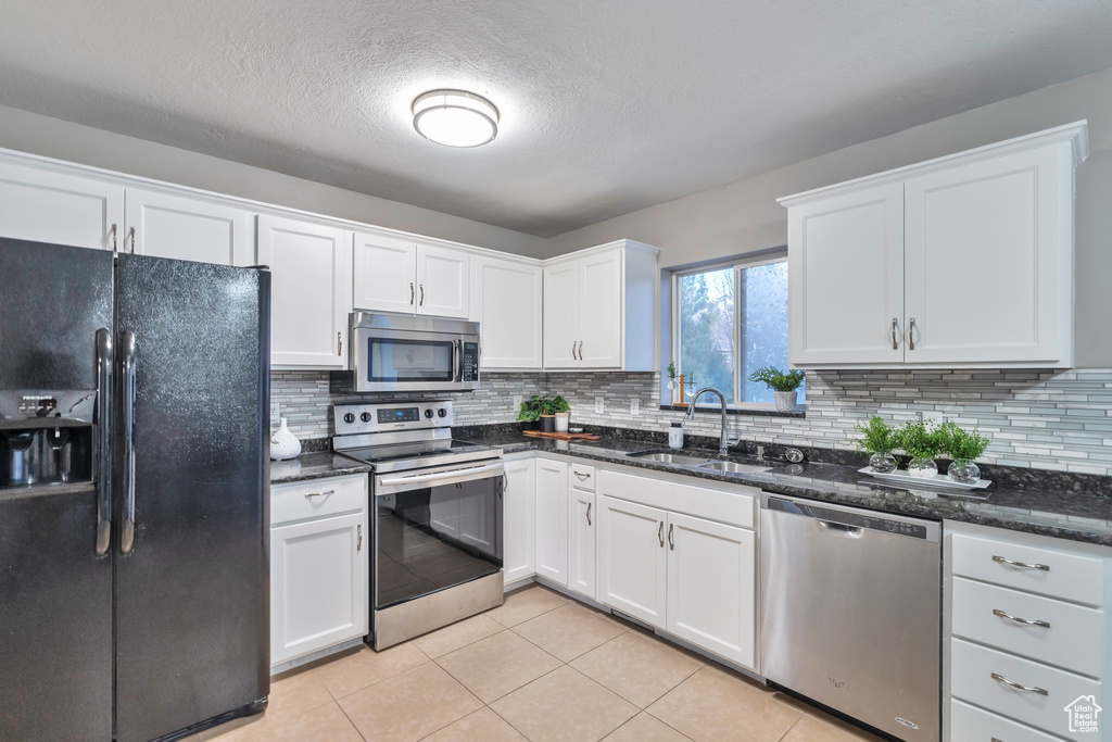 Kitchen featuring backsplash, appliances with stainless steel finishes, light tile floors, white cabinets, and dark stone counters