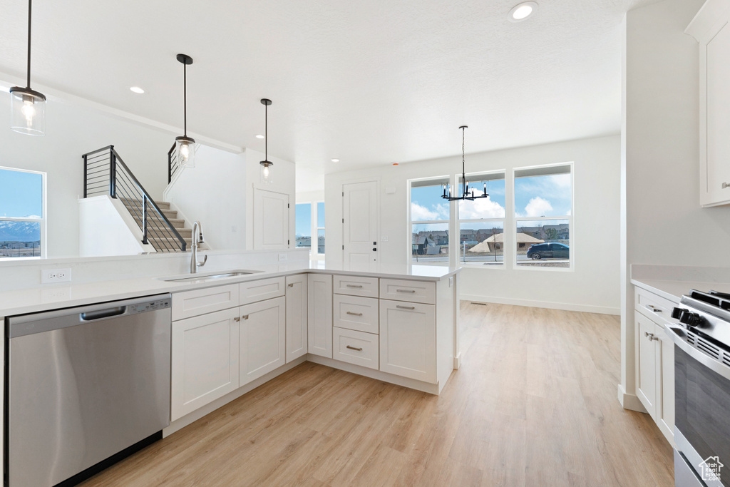 Kitchen with hanging light fixtures, light hardwood / wood-style flooring, appliances with stainless steel finishes, and a wealth of natural light