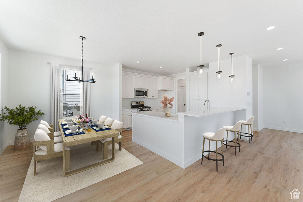 Kitchen featuring appliances with stainless steel finishes, light hardwood / wood-style flooring, white cabinets, a chandelier, and pendant lighting