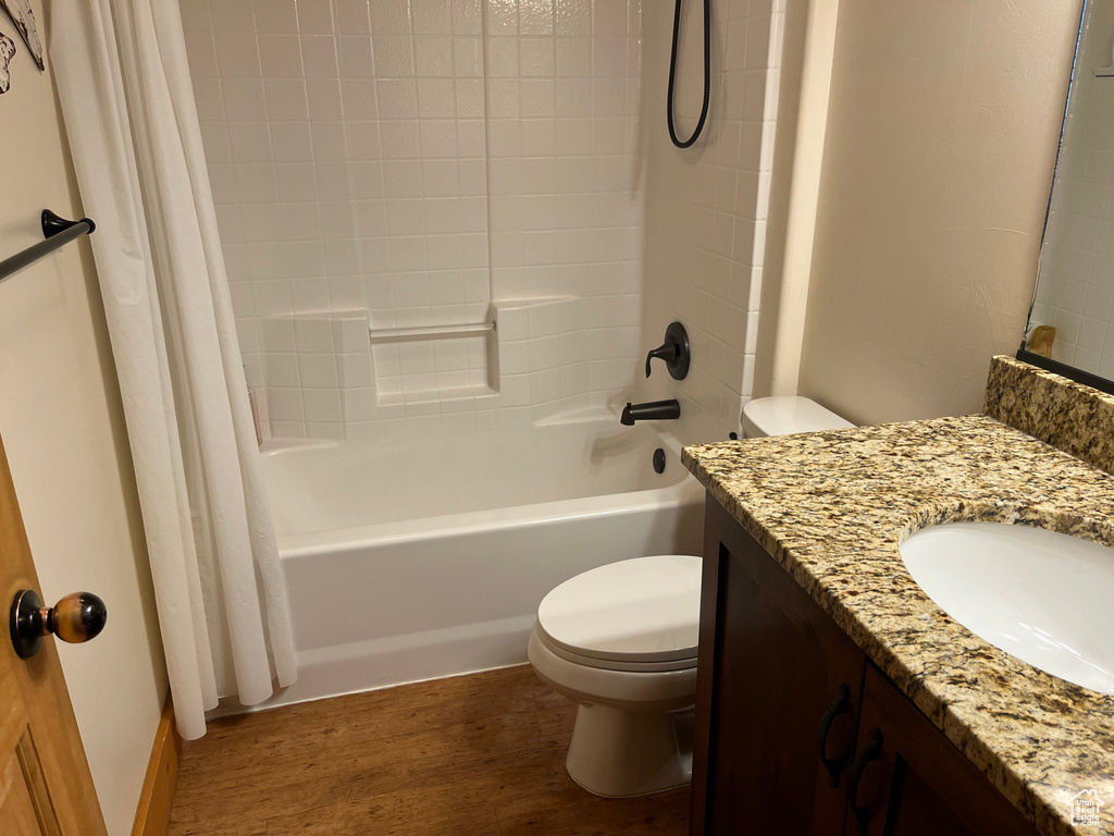 Full bathroom featuring hardwood / wood-style floors, vanity with extensive cabinet space, shower / bath combination with curtain, and toilet