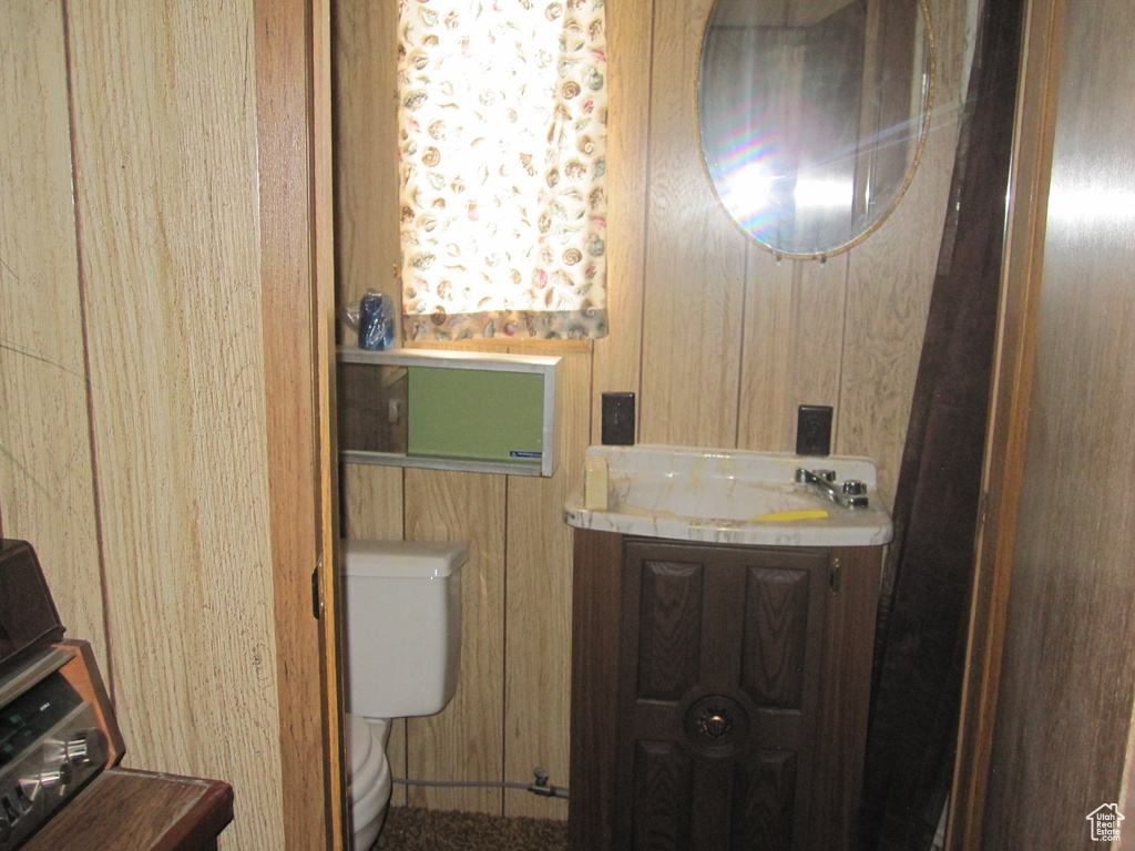 Bathroom featuring toilet, wooden walls, and vanity with extensive cabinet space