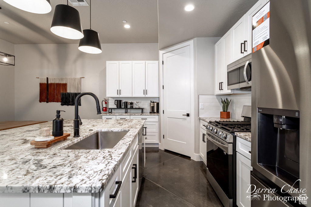 Kitchen featuring pendant lighting, white cabinets, stainless steel appliances, sink, and light stone counters