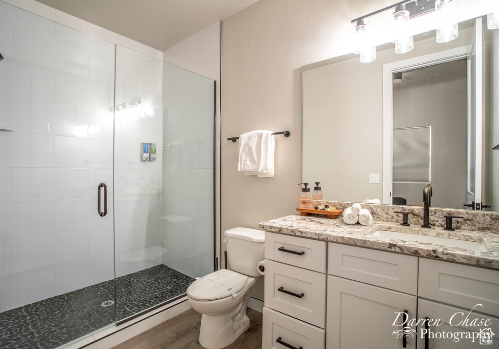 Bathroom featuring hardwood / wood-style floors, vanity with extensive cabinet space, toilet, and a shower with shower door